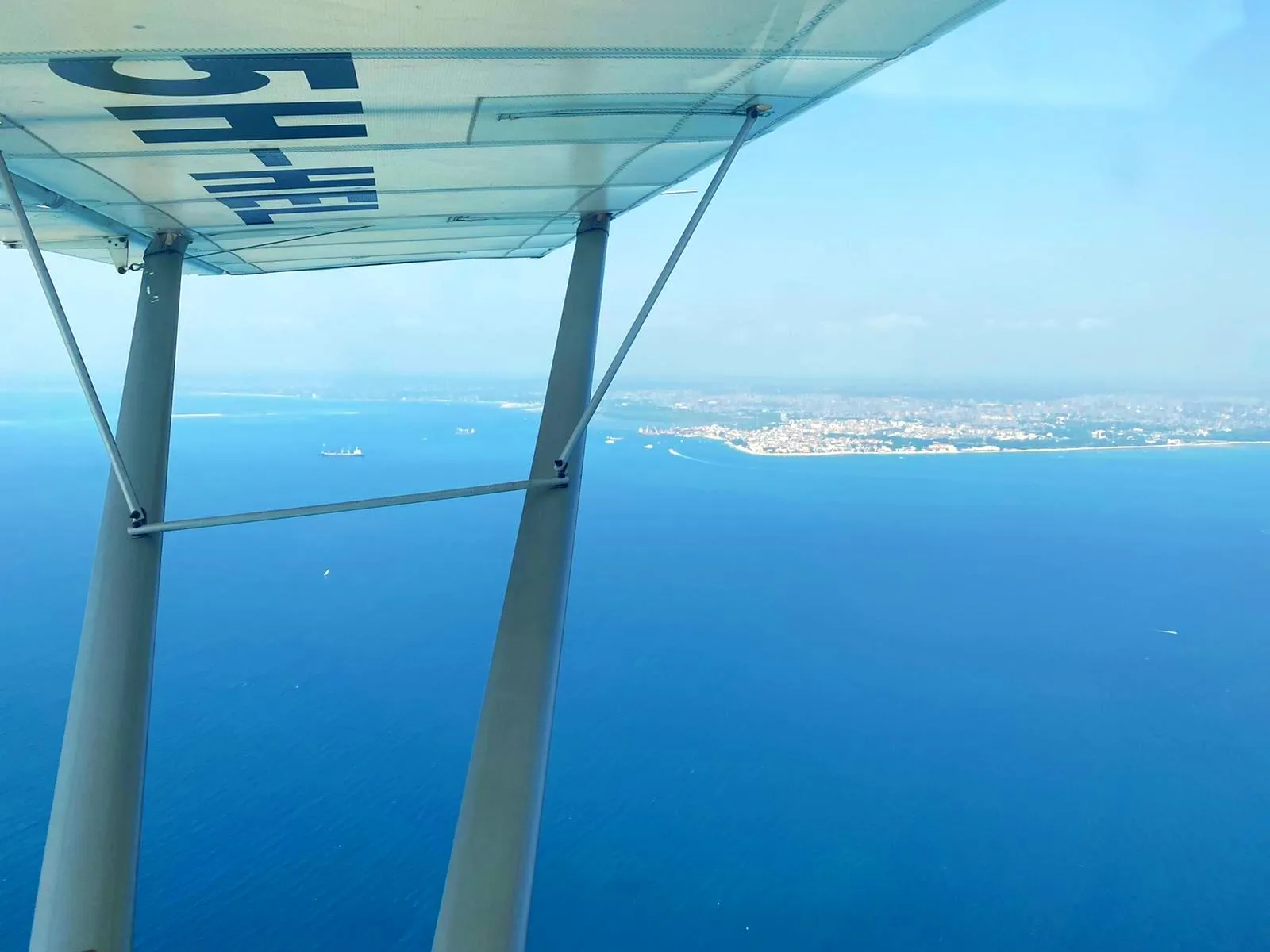 Wing and struts of a ZRP light aircraft over the Indian Ocean, approaching the coast